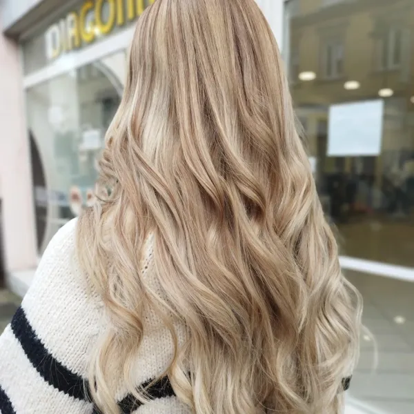Balayage blond beige lumineux sur cheveux longs ondulés, vu de dos