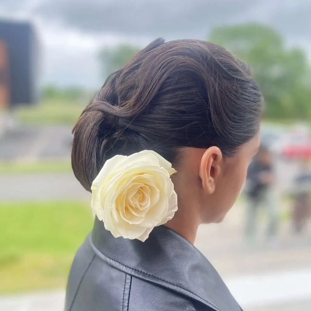 Chignon bas lissé orné d’une rose blanche, vu de profil