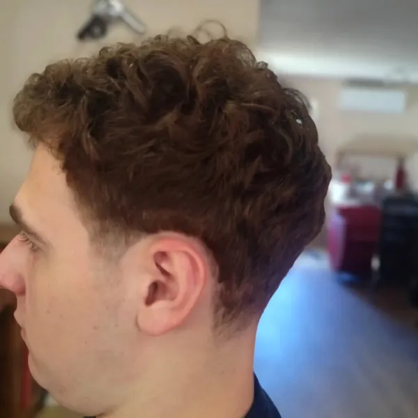 Coupe homme sur cheveux bouclés avec dégradé sur les côtés, vue de profil